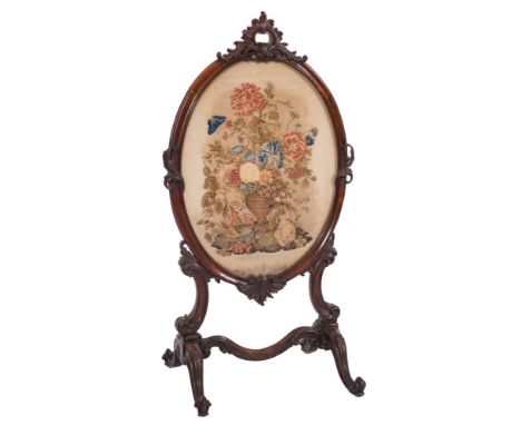 A Victorian carved rosewood oval firescreen:, with rocaille, C-scroll and acanthus leaf cresting, inset with a panel of petit