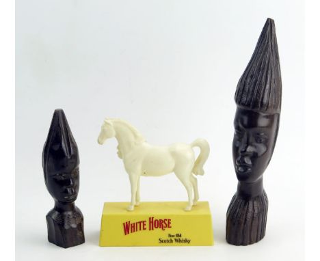 Two African carved wood busts, 26cm and 16cmmhigh, together with a plastic advertising figure for White Horse Scotch Whisky. 