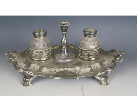 A Victorian plated ink stand, of cartouche-shaped outline, with central taper stick, flanked by clear glass ink wells, with c