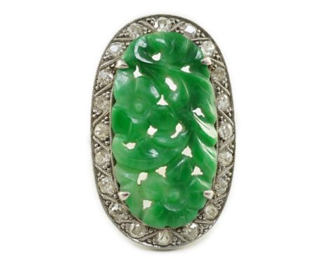 A 1920's/1930's white gold, jadeite and diamond set oval dress ring, the foliate carved jadeite, bordered by millegrain set r