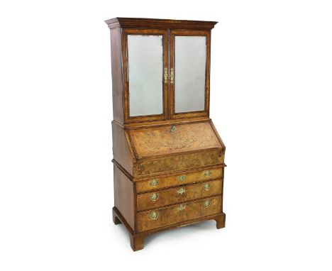 A George I walnut bureau bookcase, with moulded cornice and two bevelled mirrored doors enclosing a compartmented interior ov