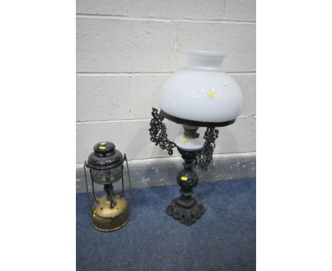 A WROUGHT IRON OIL LAMP, with an open foliate design, the glass shade supported by triple arms, over a glass reservoir, heigh
