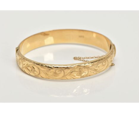 A 9CT GOLD BANGLE, a hollow domed hinged bangle, engraved with a scrolling foliage design, fitted with an integrated hook cla
