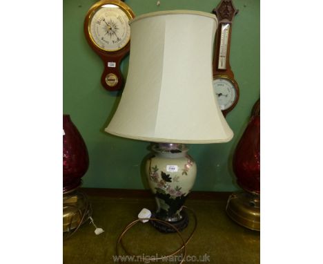 An oriental style table lamp and shade, the lamp decorated with birds and prunus on a sage green ground with wooden plinth ba