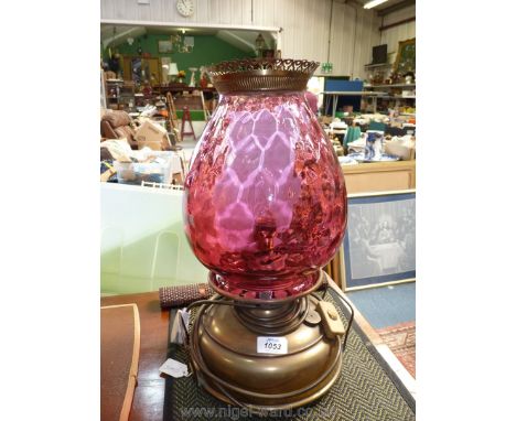 A church oil heater lamp with squat brass base, three pimple feet, converted to electric, cranberry shade and brass crown, he
