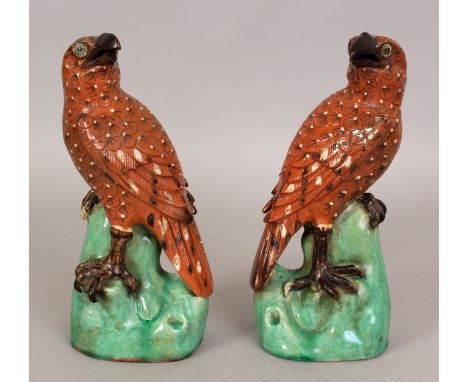 A MIRROR PAIR OF 20TH CENTURY CHINESE GLAZED CERAMIC MODELS OF FALCONS, each with turned head and perched on a rocky plinth, 