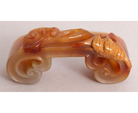 AN UNUSUAL CHINESE AGATE BRUSH REST, in the form of a low scroll footed stand decorated to its top surface with a bat and lin