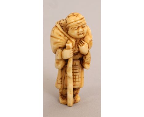 A SMALL EARLY 20TH CENTURY JAPANESE MARINE IVORY NETSUKE OF A TRAVELLER, carrying a sack over his shoulders and bearing a sta