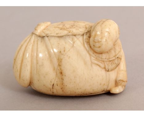 AN EARLY 20TH CENTURY SIGNED JAPANESE SECTIONAL BONE IVORY NETSUKE OF A BOY CLASPING THE SIDE OF A LARGE BAG, the base plate 