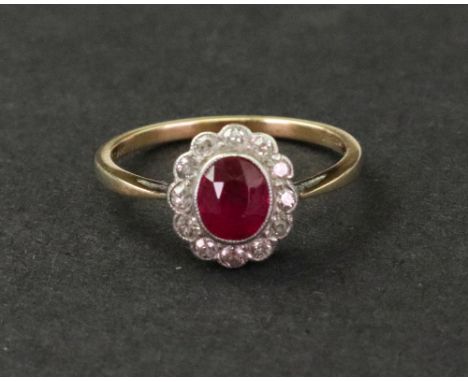 An 18ct gold, ruby and diamond-set oval cluster ring, the central oval mixed-cut ruby within a surround of twelve millegrain-