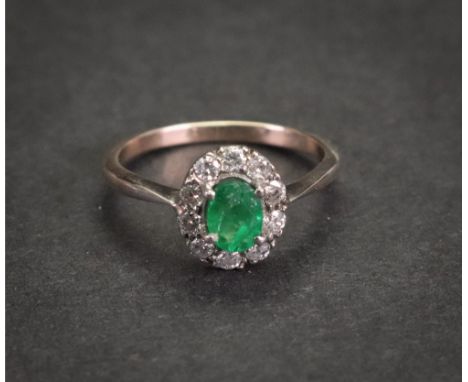 An emerald and diamond cluster ring, the oval-cut emerald claw set in a surround of circular-cut diamonds, mounted in yellow 