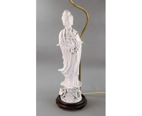 A Chinese blanc de chine figure of guanyin, 20th century, holding a lotus flower, mounted as a table lamp, with shade, the fi
