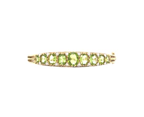 A VICTORIAN STYLE HINGE BANGLE, SET WITH NINE GRADUATED OVAL GREEN PERIDOT. BUTTON CLASP WITH SAFETY CHAIN AND FIGURE EIGHT L