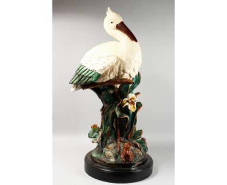 A LARGE MAJOLICA STORK STICK STAND, standing beside an open flower, on a circular base. 40ins high.