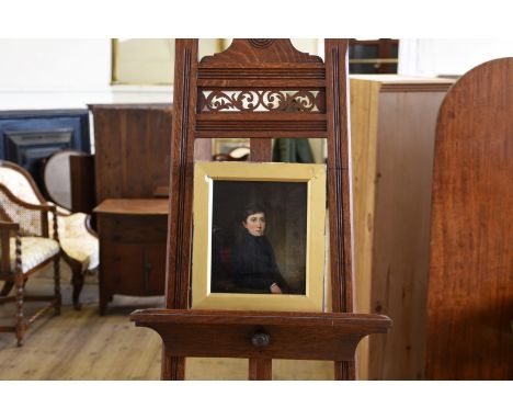 A 19th century oil on canvas portrait of a young boy wearing a black overcoat and with his elbow on a green baize table with 