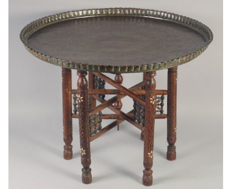 A LARGE 19TH CENTURY PERSIAN BRASS TRAY TABLE, the tray engraved with panels of figures, with mother of pearl inlaid wooden s