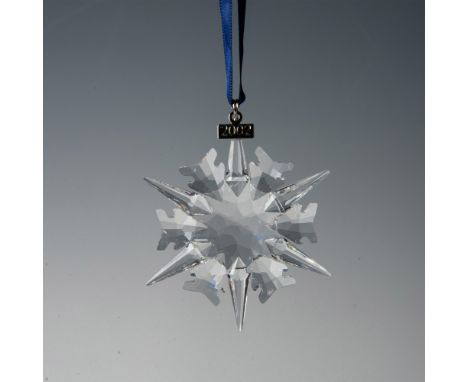 A clear, faceted six point snowflake adornment featuring a metal tag with 2002 impressed on it, hanging from a navy blue ribb