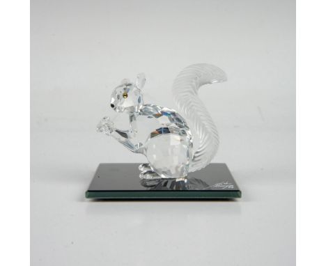 A clear faceted figure of a squirrel with a black nose, iridescent black eyes, a textured frosted tail and holding a crystal 