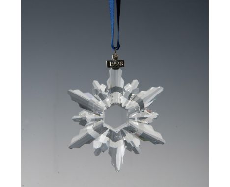 A clear, faceted twelve-point snowflake ornament, hanging from a satin navy blue ribbon, with a metal tag impressed with 1998