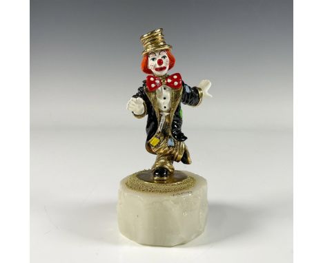 A gilded enamel figure of a clown in a large black jacket with colorful patches and a red polka dot bow tie. Presented on a w