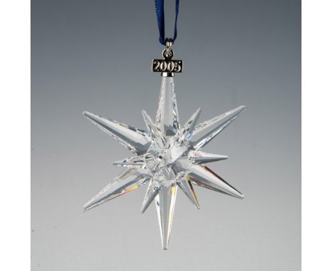 A clear, faceted snowflake adornment featuring a metal tag with 2005 impressed on it, hanging from a navy blue satin ribbon. 