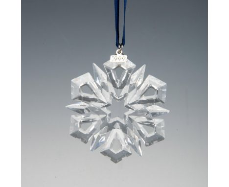 A clear, faceted twelve pointed snowflake adornment featuring a metal tag with 1999 impressed on it, hanging from a navy blue