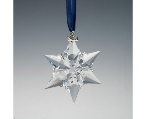 A clear, faceted six point snowflake adornment featuring a metal tag with 2000 impressed on it, hanging from a navy blue ribb