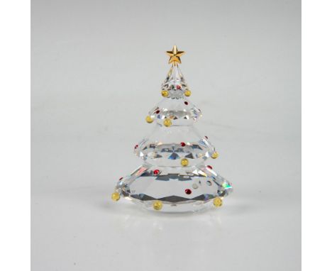 A clear faceted figure of a holiday tree, adorned with a gold-colored metal star and red and yellow crystals. Part of the Exq
