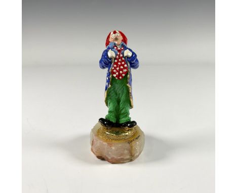 A gilded enamel figure of a clown wearing a polka dot red tie and green pants, gazing upwards. Presented on a white onyx ston