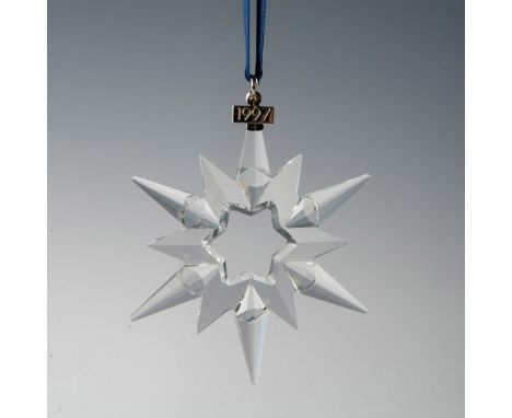 A clear, faceted twelve-point snowflake ornament, hanging from a satin navy blue ribbon, with a metal tag impressed with 1997