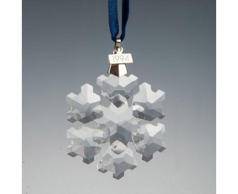A clear, faceted snowflake adornment featuring a metal tag with 1994 impressed on it, hanging from a satin navy blue ribbon. 