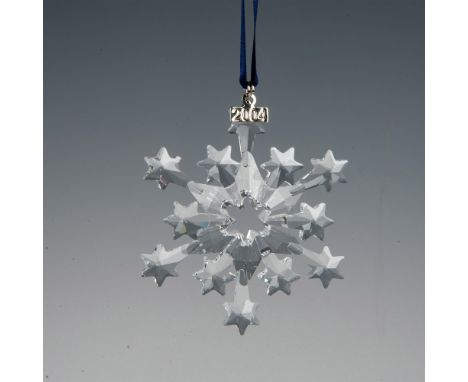 A clear, faceted star snowflake adornment featuring a metal tag with 2004 impressed on it, hanging from a navy blue satin rib