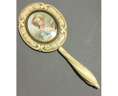 A 19th century carved ivory lady's dressing table mirror, the back inset with a miniature portrait of a young lady gathering 