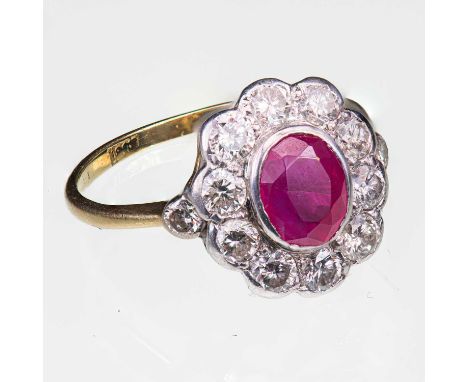 AN EDWARDIAN STYLE RUBY AND DIAMOND CLUSTER RING marked '18CT', set with an oval-cut ruby, within a border of ten round brill