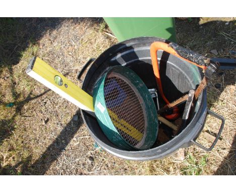 A black dustbin of garden tools, sledge hammer, saw, etc.