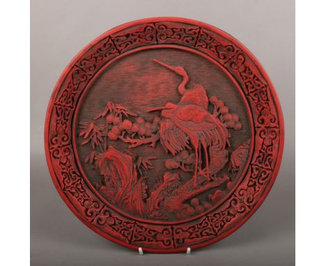 A Chinese cinnabar style dish. Decorated in relief with cranes in a landscape with pine trees. Kangxi reign mark to the rever