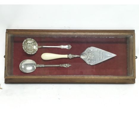 Glazed case containing decorated bricklaying Trowel and two large decorative spoons
