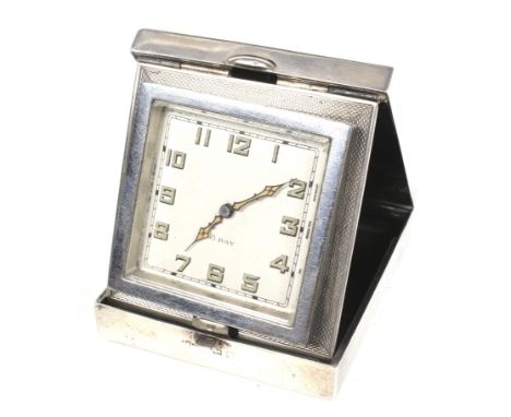 A George V silver and enamel cased travel clock. The square dial with Arabic numerals and an eight day movement. The case mar