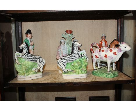 A pair of Staffordshire flatback figures of zebras, a lustre decorated cow creamer, a standing double sided gin/water figure,