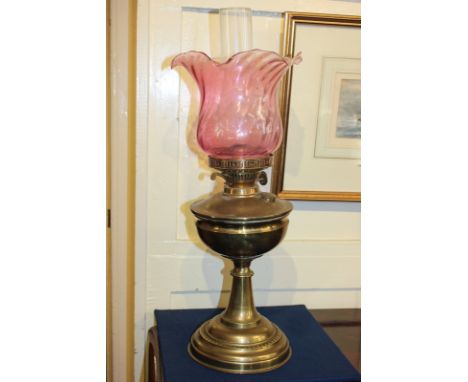 A brass oil lamp, with glass funnel and cranberry coloured shade 56cm