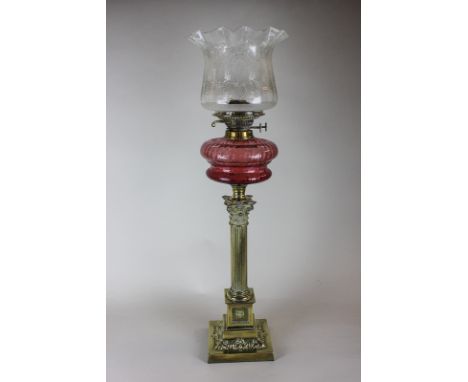 A Victorian oil lamp, the embossed brass column supporting a cranberry glass well with burner and etched clear glass shade, 7