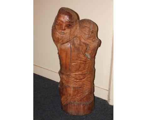 A roughly carved sculpture in the form of a man's head emerging from a tree trunk, 81cm high