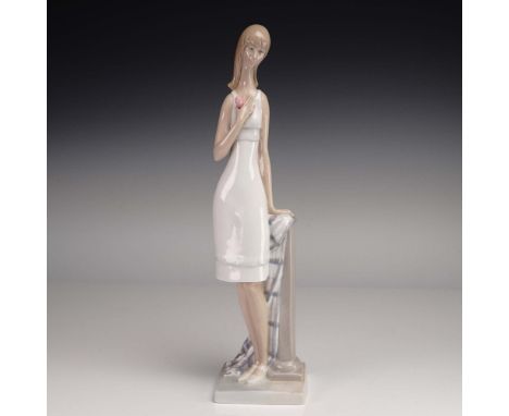 Lladro porcelain figurine 01001028, titled Girl with Heart, is a graceful representation of a young woman in a simple white d