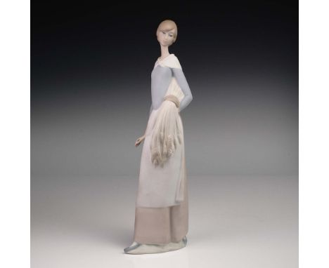 This early Lladro porcelain figurine, Woman with Wheat, depicts a slender young woman in a pale blue blouse and apron, gracef
