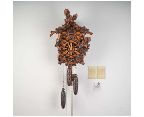 This intricately hand-carved Black Forest cuckoo clock by Fehrenbach features a traditional chalet-style case adorned with fi