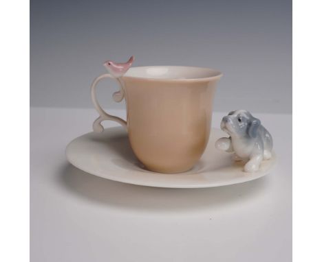 This charming porcelain cup and saucer set features a pastel peach cup with a delicate handle accentuated by a pink bird perc