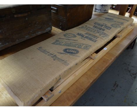 A long narrow folding wooden garden bench with sacking covered cushion