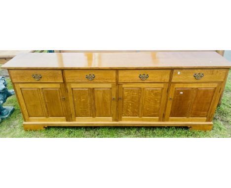 A 20th Century light oak sideboard, four frieze drawers with batwing brass handles over four panel cupboards, raised on brack