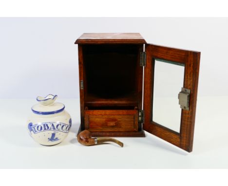 An oak smokers cabinet with single glazed door, blue and white ceramic tobacco jar to the interior with single drawer and pip