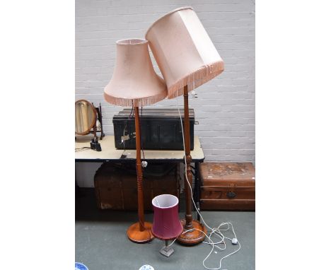 Two standing lamps with turned bases and light pink shades and a bedside lamp